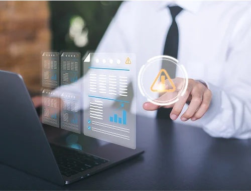 A person in business attire uses a laptop while interacting with virtual data screens and a warning icon, suggesting cybersecurity or data risk management.