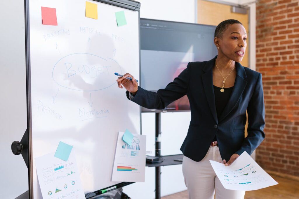 A person in business attire stands by a whiteboard presenting budget plans, highlighting how to hire virtual CFO services. The whiteboard displays notes and diagrams related to budget strategy in a meeting room.
