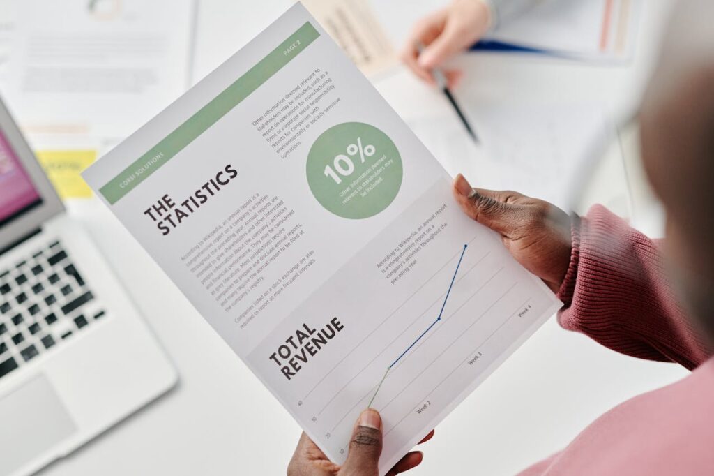 A person holds a printed statistics report featuring a 10% increase graphic and total revenue line chart, with a laptop and paperwork on the desk—demonstrating the insights you gain when you hire virtual CFO services.