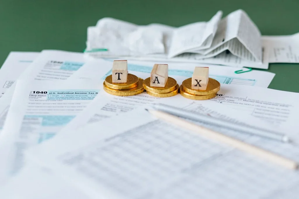 Tax documents, receipts, a pencil, and stacked gold coins with letter tiles spelling "TAX" arranged on a desk, representing financial paperwork and tax preparation assisted by CFO outsourcing services.